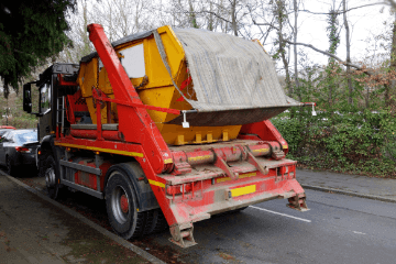 Red skip lorry delivering a skip on the road